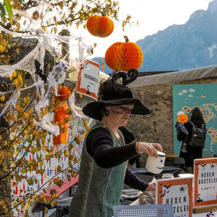 A lion in a costume holds a glowing pumpkin in its hand. It is a nighttime scene with dim light and trees in the background. | © Zoo Salzburg Hellbrunn