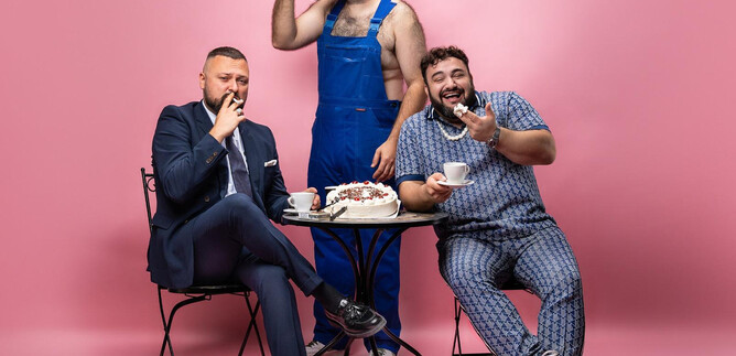 Three men are sitting at a table in front of a pink wall. One is drinking coffee while the others are enjoying sweets. | © Home of Content GmbH