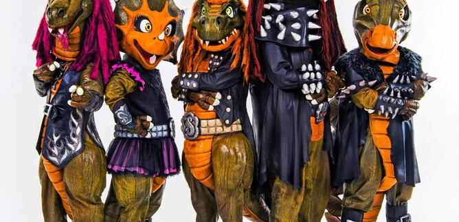 A group of dinosaur mascots in rockin' outfits stands in front of a dramatic background landscape. The text "Heavy Saurus" is prominently placed. | © sonymusic.de