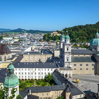An impressive view of the city of Salzburg with its historic buildings and green hills. The clear sky and the architecture create a picturesque scene. | © TSG Toursimus Salzburg