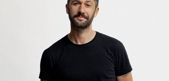 A man stands in front of a neutral background. He is wearing a black t-shirt and has a light beard. | © Susan Buth