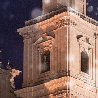 A beautiful tower illuminated at night, surrounded by snowflakes. In the foreground, a Christmas tree is visible. | © Universität Mozarteum