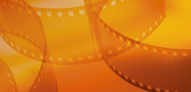 An orange background with film strips elegantly layered on top of each other. The scene conveys a sense of creativity and cinematography. | © Shutterstock_Serhii Yushkov
