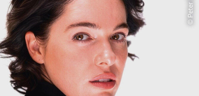 A portrait of a woman with short, dark hair and natural makeup. She looks directly at the camera and has a neutral facial expression. | © Peter Müller