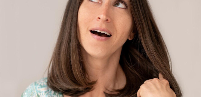A woman with long, brown hair is pointing her finger upwards and looks surprised. She is wearing a colorful top and has a friendly expression. | © lynephotography.com