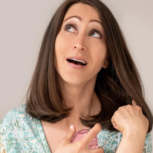 A woman with long, brown hair is pointing her finger upwards and looks surprised. She is wearing a colorful top and has a friendly expression. | © lynephotography.com