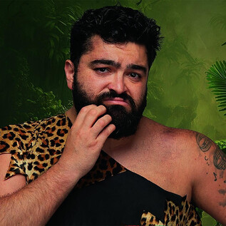 A man in a leopard skin with a thoughtful expression. In the background, green plants and jungle can be seen. | © Serdar Karibik