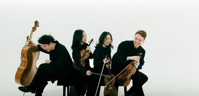 A group of four musicians is seated, dressed in black. They are playing various string instruments and appear to be cheerful. | © Co Merz