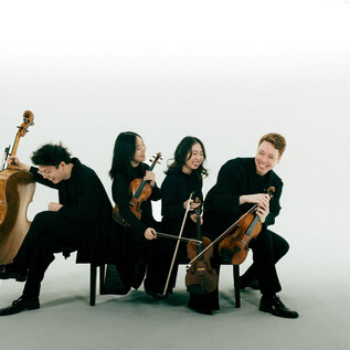 A group of four musicians is seated, dressed in black. They are playing various string instruments and appear to be cheerful. | © Co Merz