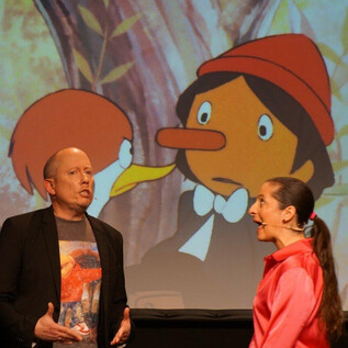 A live performance with two performers on stage. In the background, a scene from an animated film can be seen. | © Sole Goscinski
