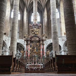 An impressive church with tall columns and an ornate altar in the background. The rays of light pour through the windows, creating a peaceful atmosphere. | © TSG_B. Brunauer