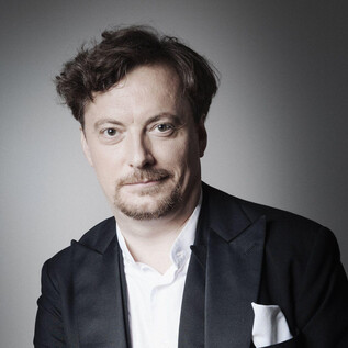 A man in an elegant suit with a white shirt and a white pocket square. The background is gray and neutral. | © Anita Schmid