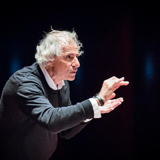 An older man with gray hair is gesticulating passionately during a speech. He is wearing a dark gray sweater and looks engaged. | © Franois Volpe