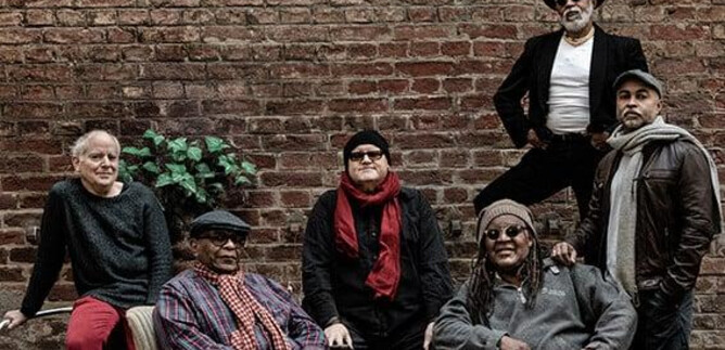 A group of six men is sitting and standing in front of a brick wall. They are wearing different clothes and posing relaxed in the scene. | © Jan Scheffner
