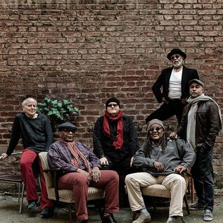 A group of six men is sitting and standing in front of a brick wall. They are wearing different clothes and posing relaxed in the scene. | © Jan Scheffner