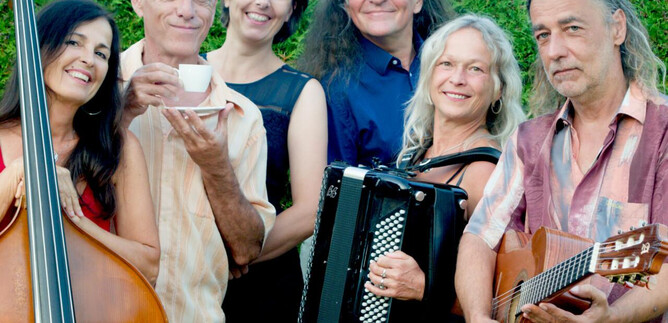 A group of six musicians stands together and smiles at the camera. They are holding various instruments and a cup in their hands. | © MÉLANGE