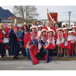 A group of people in festive attire stands in front of a float. They are celebrating a parade and appear cheerful. | © Salzburger Faschingsgilde