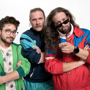 Three men in colorful sports jackets pose together. They have various accessories and facial expressions that convey a casual and confident impression. | © Prenninger