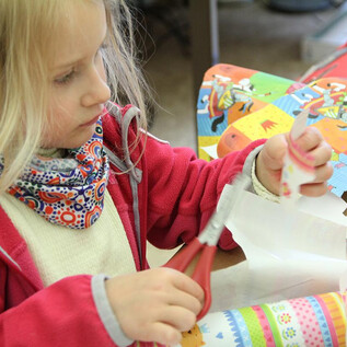 A collection of colored pencils and scissors in metal containers. In the foreground, orange bowls are visible. | © DomQuartier