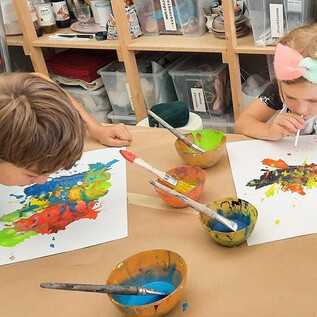 Zwei Kinder sitzen an einem Tisch und malen mit bunten Farben. Vor ihnen stehen Schalen mit Farben und ihre Kunstwerke auf Papier. | © DomQuartier