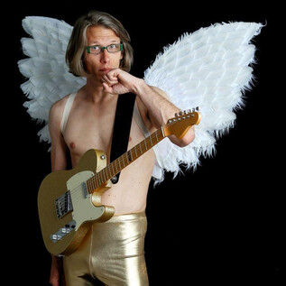 A man with angel wings holds a guitar and looks contemplative. He is wearing golden pants and has a unique hairstyle. | © Volker Weihbold