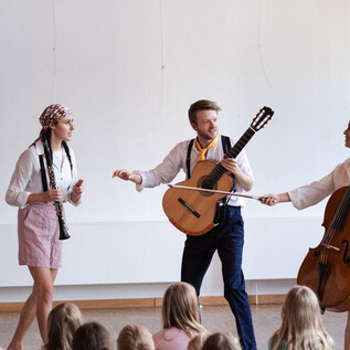 A lively music performance with three artists on stage. The audience, predominantly children, watches attentively. | © Jakob Schad