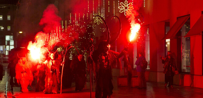 A crowd with bengal flares is celebrating in a festively lit street. Red lights create a lively and festive atmosphere. | © Sternadvent