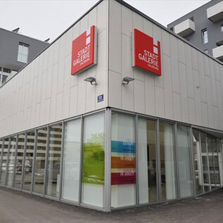 A modern business complex with large glass windows. The building features a red sign that reads "City Gallery". | © Stadtgemeinde Salzburg