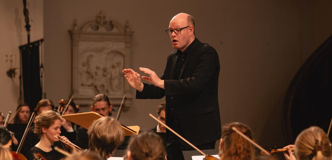 A musical performance in a festively decorated church. Four musicians play in front of an audience, surrounded by fir trees and colorful lights. | © Simone Both