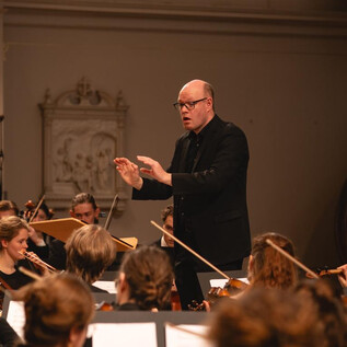 A musical performance in a festively decorated church. Four musicians play in front of an audience, surrounded by fir trees and colorful lights. | © Simone Both