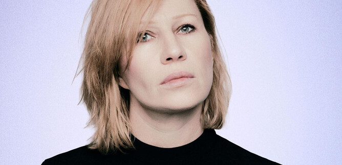 A person with blonde, slightly messy hair is looking thoughtfully into the distance. They are wearing a black top against a soft, light background. | © Susanne Hassler-Smith