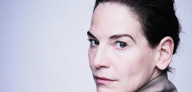 A woman looks over her shoulder. Her face has a serious expression and she is wearing an elegant blouse. | © Burgtheater