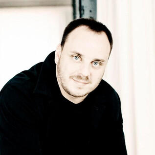 A man with short hair stands in a bright room. He has a friendly expression and is wearing a black top. | © Marco Borggreve