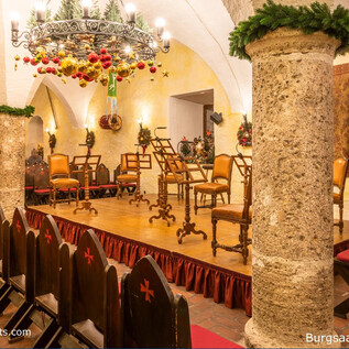 A beautiful hall with wooden chairs and a festive chandelier. The walls are decorated and create a welcoming atmosphere. | © salzburghighlights