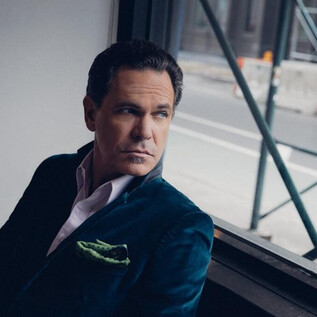 A contemplative man sits by the window and gazes outside. He is wearing an elegant suit and has a stylish demeanor. | © Anna Webber