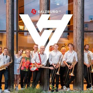 A group of musicians stands in front of a modern building with a wooden facade. They are holding various musical instruments and smiling at the camera. | © Rockhouse Salzburg