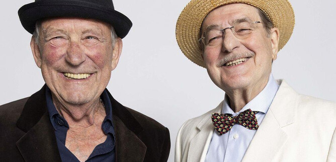 Two older men are smiling happily at the camera. The first one is wearing a black hat, while the second is wearing a light straw hat and an elegant jacket. | © Xenia Trampusch