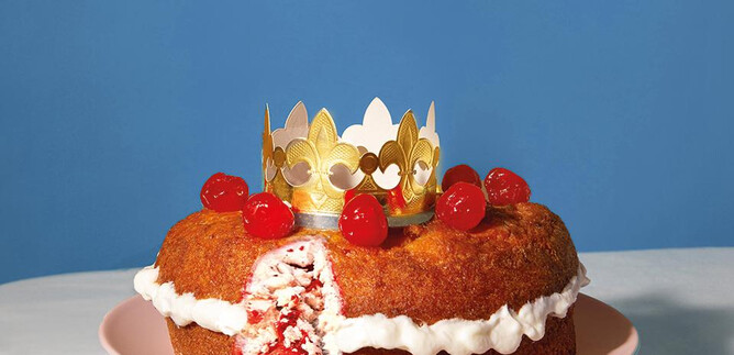 Un hermoso pastel en un plato, decorado con una corona dorada y cerezas. El pastel tiene un relleno afrutado y se ve apetitoso. | © Valentina Schuster