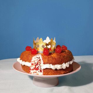 Ein schöner Kuchen auf einem Teller, dekoriert mit einer golden Krone und Kirschen. Der Kuchen hat eine fruchtige Füllung und sieht appetitlich aus. | © Valentina Schuster