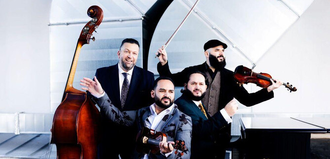 A group of four musicians playing various instruments, including a double bass and a violin. They are wearing elegant suits and are posing together in a modern space. | © Julia Wesely