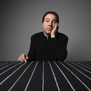 A pensive man sits at a table with black and white stripes. He has one hand on his face and looks serious. | © Fethi Karaduman