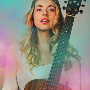 A young woman with blonde curls holds an acoustic guitar. She has a confident smile and is wearing a simple top. | © Christian Verch