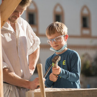 An adult and a child are working together on a rock block. The child is wearing safety glasses and holding a hammer in their hand. | © Salzburger Burgen & Schlösser