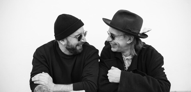 Two men are laughing and looking at each other friendly. They are wearing sunglasses and stylish hats. | © Daniela Matejschek