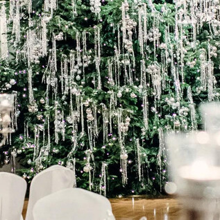 An elegant banquet hall with a decorated Christmas tree in the background. Tables are adorned with white tablecloths and candle holders. | © St. Peter Stiftskulinarium
