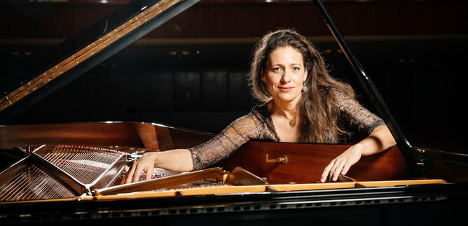 A talented pianist sits at an open grand piano in a concert hall. Her gaze is focused and she radiates enthusiasm for the music. | © Guillaum Perret