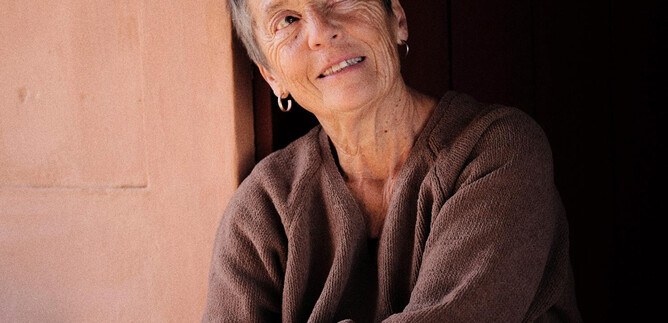 A smiling woman sits relaxed in a room with warm colors. Her gaze is thoughtful and friendly. | © Fabio Cunha