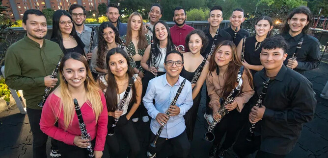 A group of young musicians stands together holding clarinets. In the background, city buildings and trees are visible. | © Daniel Romero_Iberacademy