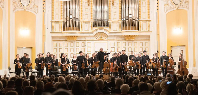 An orchestra on stage with a variety of musicians and instruments. In the background, one can see an impressive organ and an audience that is applauding. | © Wolfgang Lienbacher