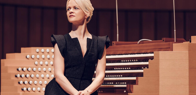 A woman sits at an organ and gazes thoughtfully into the distance. The organ has a modern design with many keys and knobs. | © Ko Cheng Lin